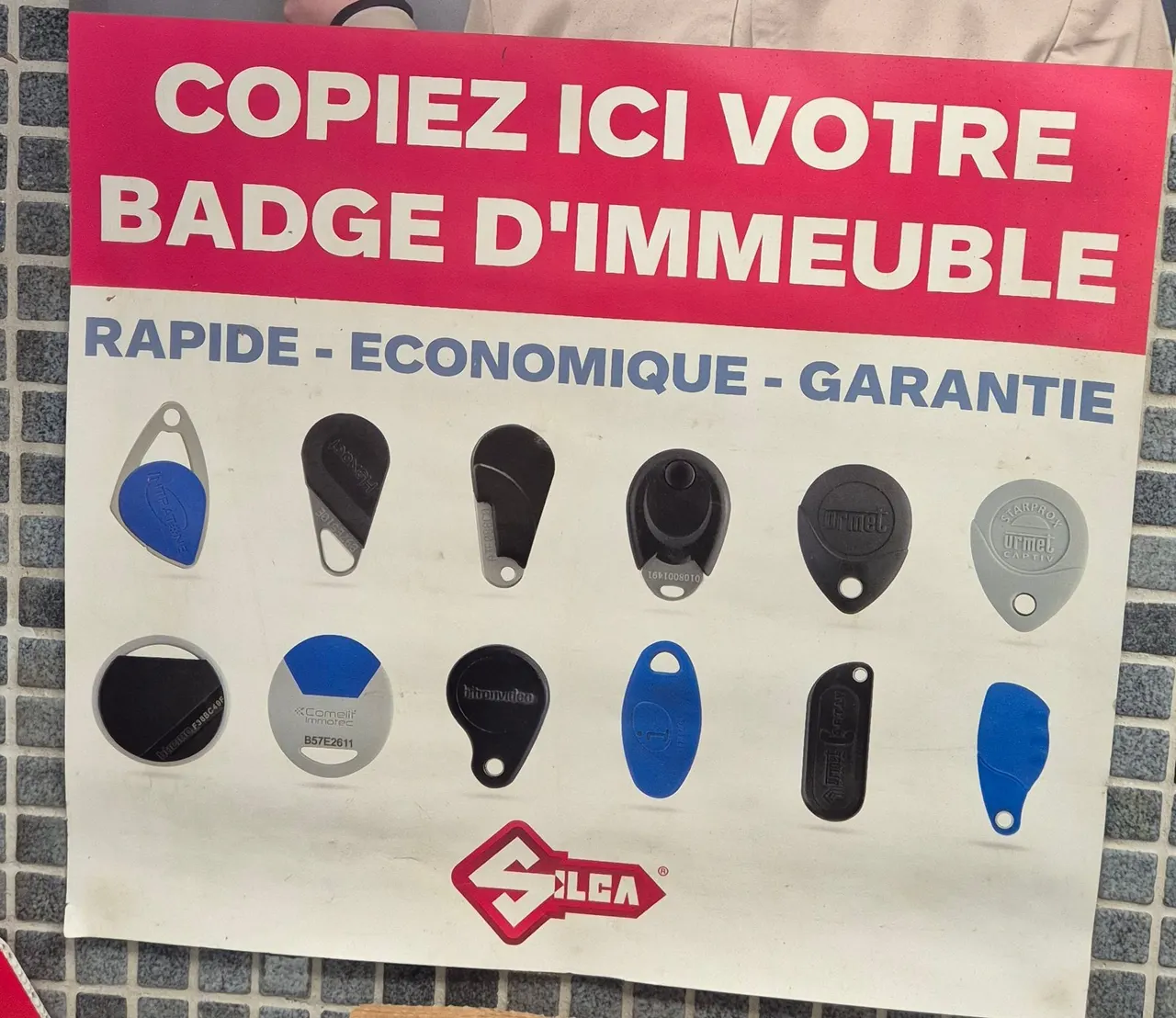 Affiche « Copiez ici votre badge d'immeuble » et éventail de badges reproduits en boutique